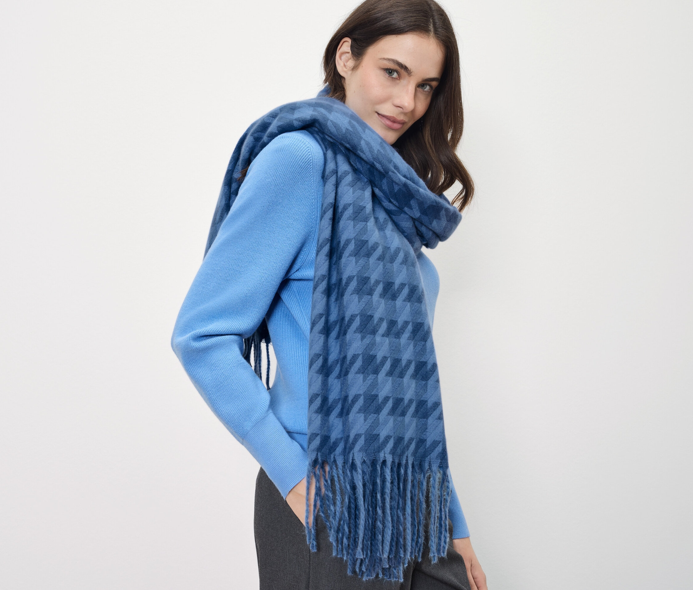 Kahverengi saçlı bir kadın mavi bir kazak ve mavi kareli bir eşarp giyiyor.