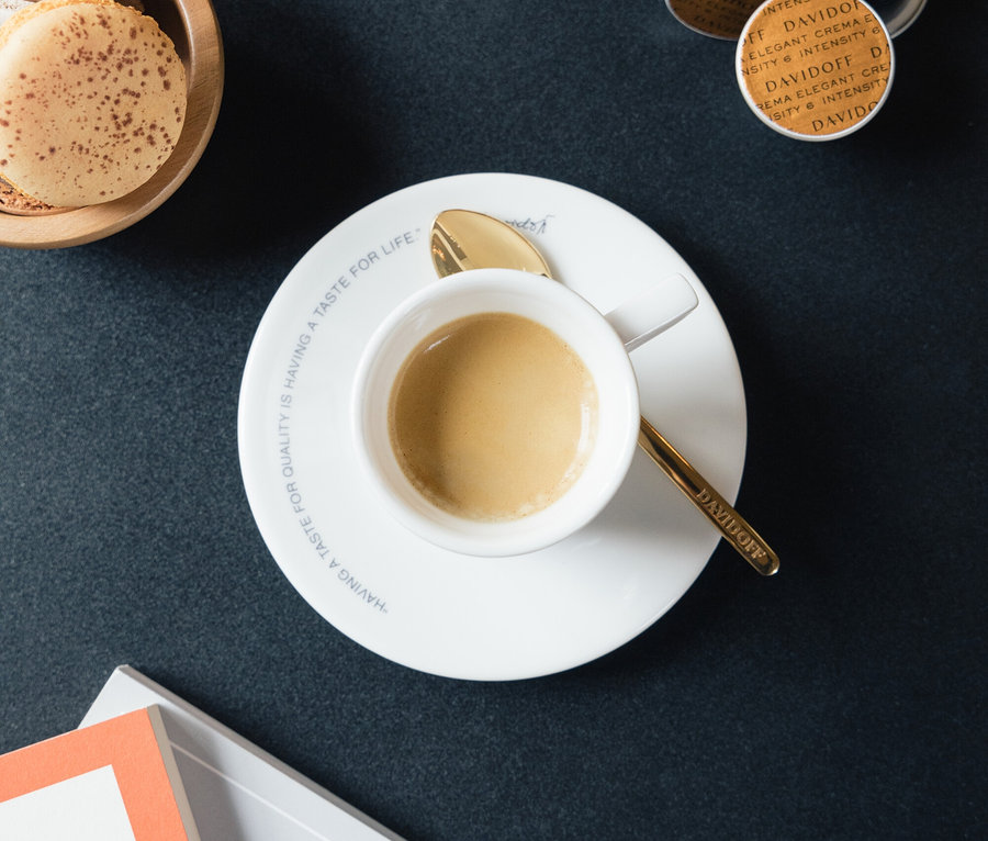 Makaronlar, kapsüller ve kitapların yanında beyaz fincan, tabak ve altın kaşık ile espresso.