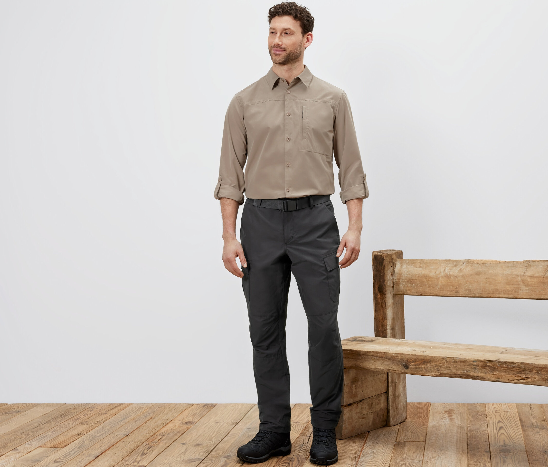 Adam sivrisinek korumalı outdoor pantolonu, bej gömleği ve siyah ayakkabıları ile ayakta duruyor.