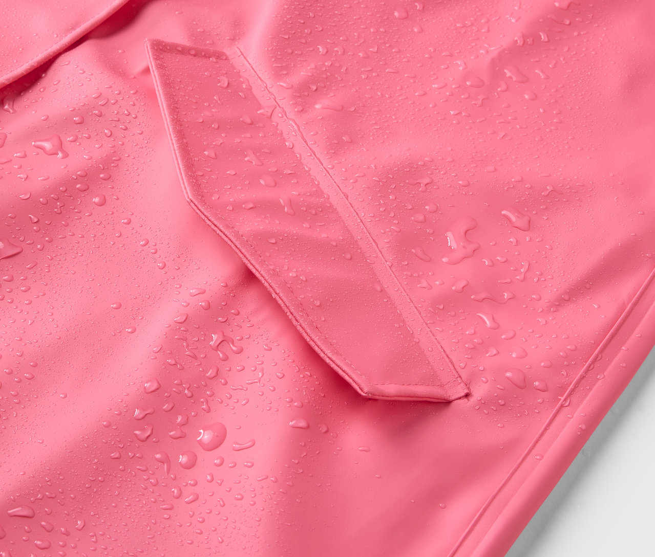 Su damlaları olan pembe bir yağmurluğun yakın çekimi.