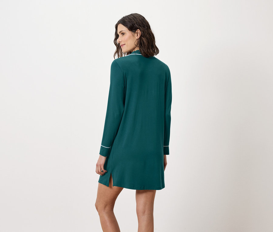 Kadın kameraya arkası dönük duruyor, uzun kollu ve beyaz şeritli zümrüt yeşili bir gecelik giyiyor.