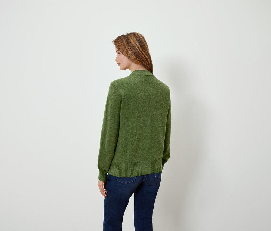 Omuzunun üzerinden bakan bir kadın, üzerinde yeşil bir kazak ve kot pantolon var.