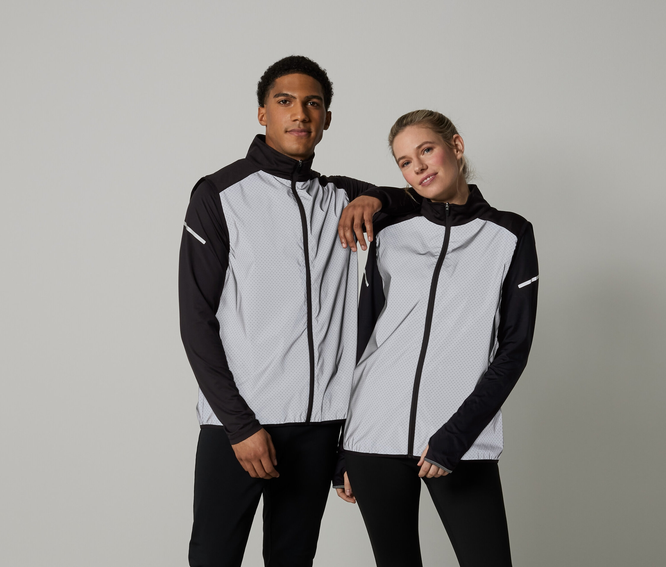 Bir erkek ve bir kadın, uzun kollu, fermuarlı ceketler içinde poz veriyorlar.