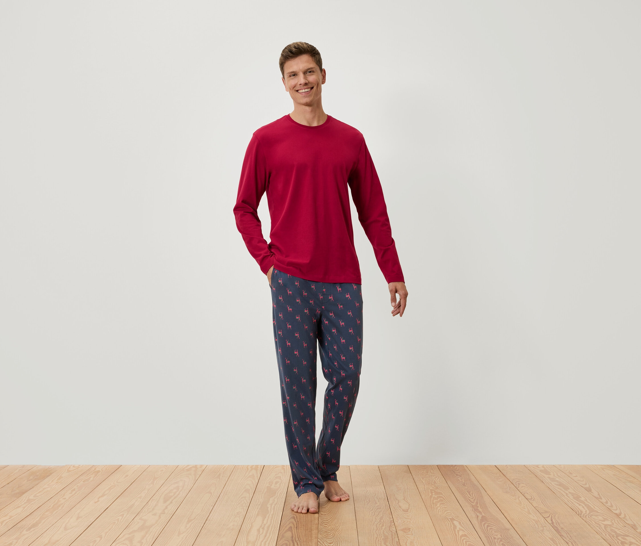 Adam yerde duruyor, üzerinde uzun kollu kırmızı bir tişört ve desenli mavi bir pijama altı var.