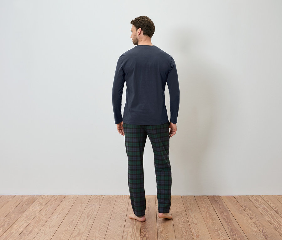 Arkası dönük bir adam lacivert pijamasını ve ekose desenli pijama altını giyiyor.