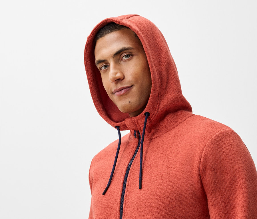 Turuncu kapüşonlu ve lacivert fermuarlı bir sweatshirt giyen bir adamın portresi.