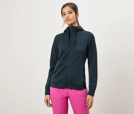 Kadın, koyu yeşil, fermuarlı kapüşonlu bir sweatshirt ve pembe pantolon giyiyor.