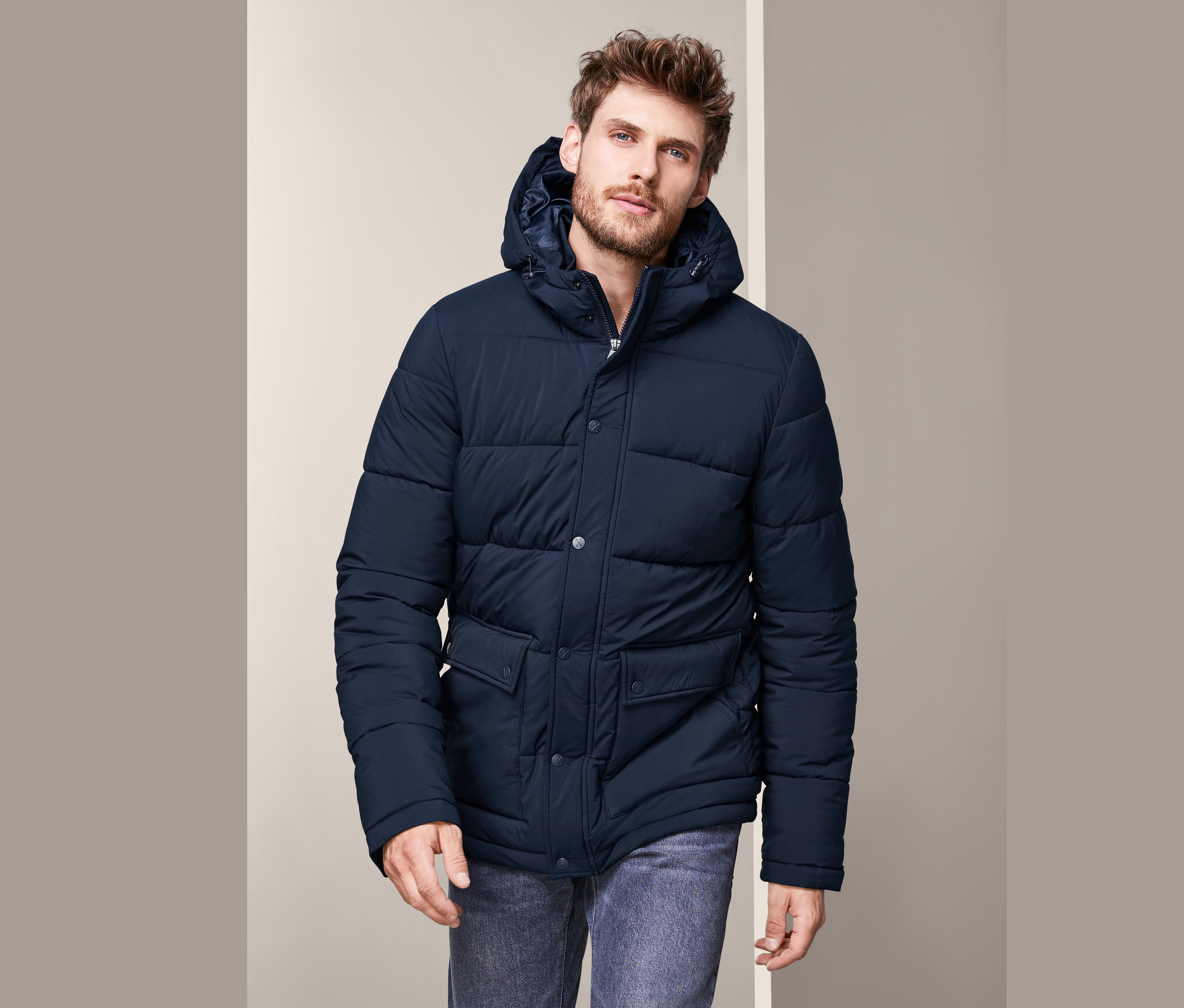 Adam Termal Kapitone Mont ve kot pantolon giyiyor.