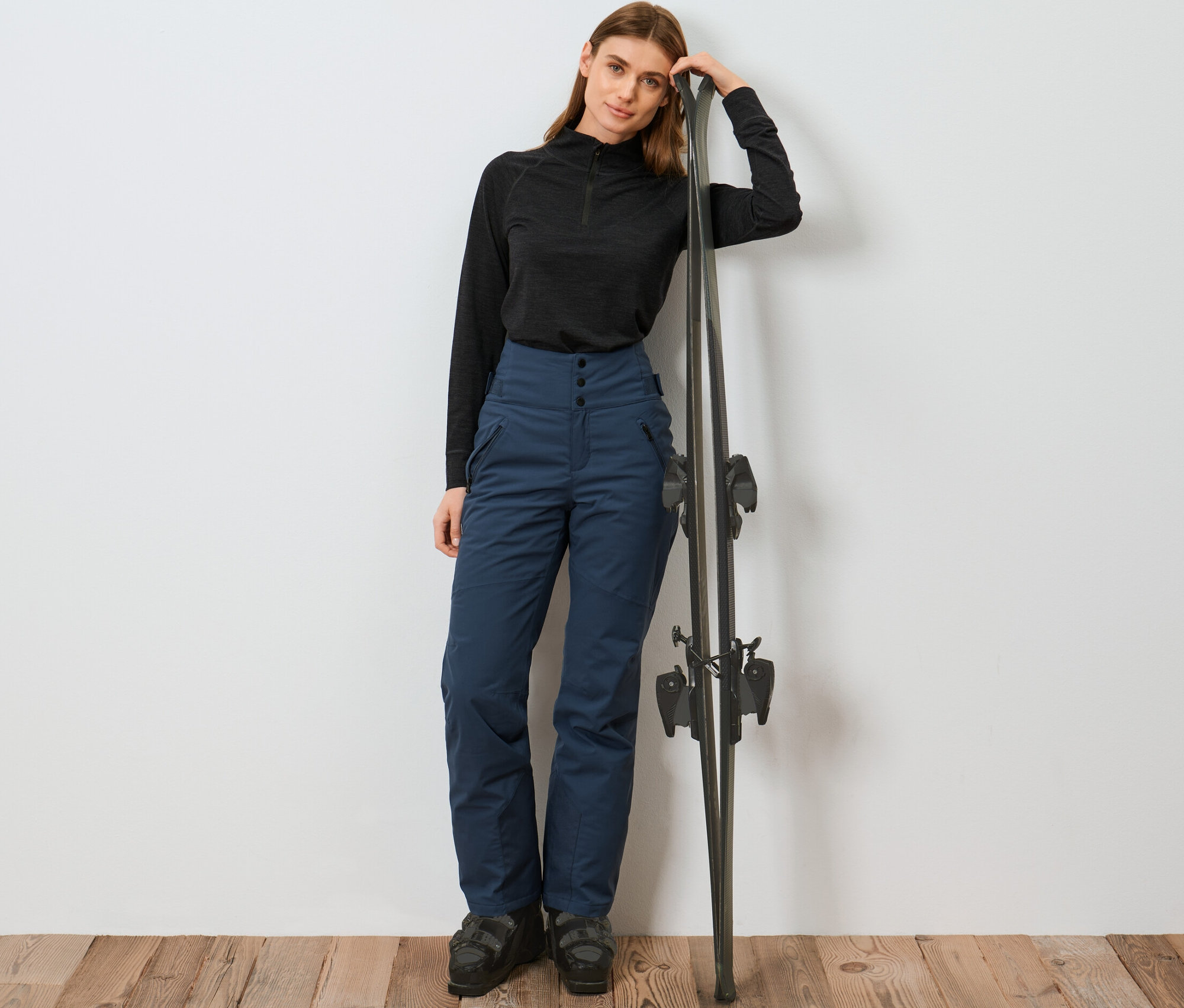 Kayaklara yaslanan kadın mavi yüksek bel kayak pantolonu giyiyor.