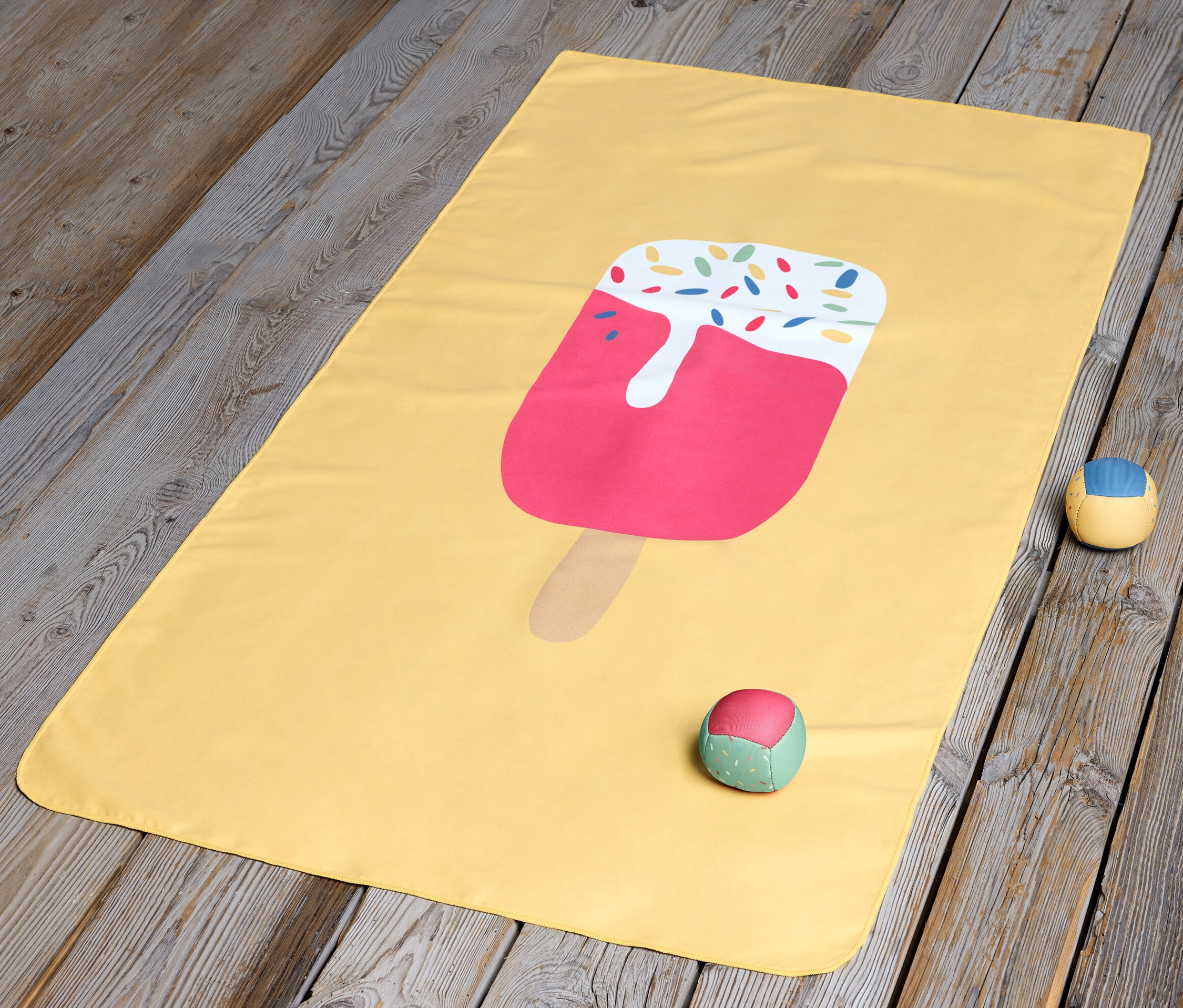 Ahşap zemin üzerinde dondurma desenli sarı bir çocuk mikrofiber havlu duruyor.