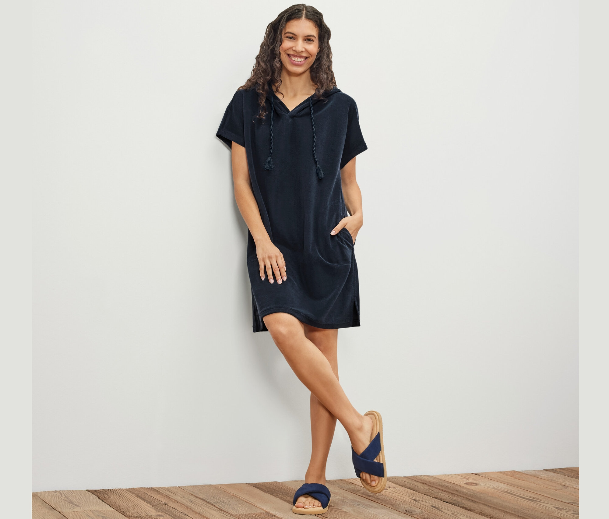 Bir duvarın önünde poz veren kadın, mavi havlu kumaş plaj elbisesi giyiyor.