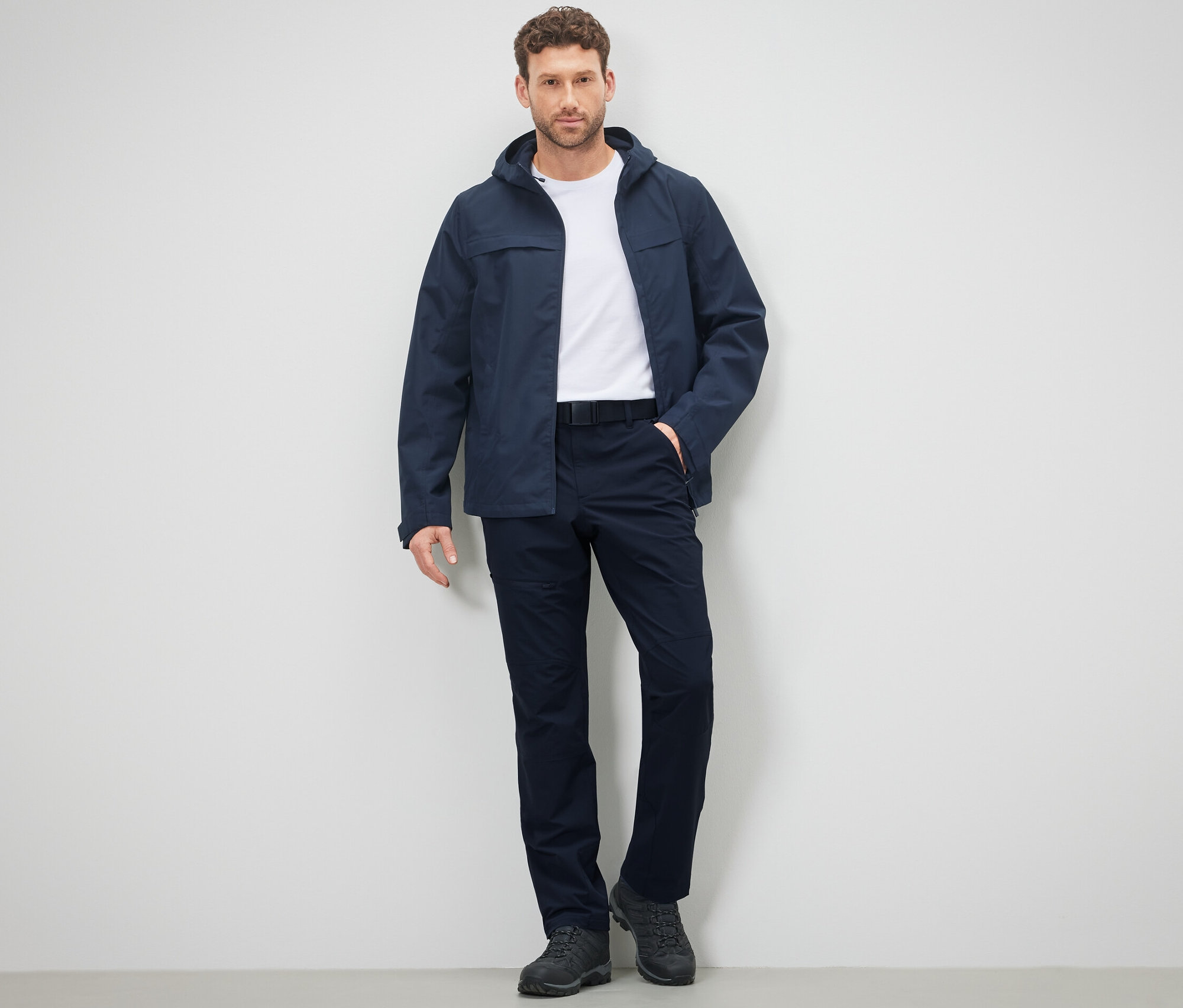 Adam duvara karşı açık hava pantolonu ve ceketle poz veriyor.