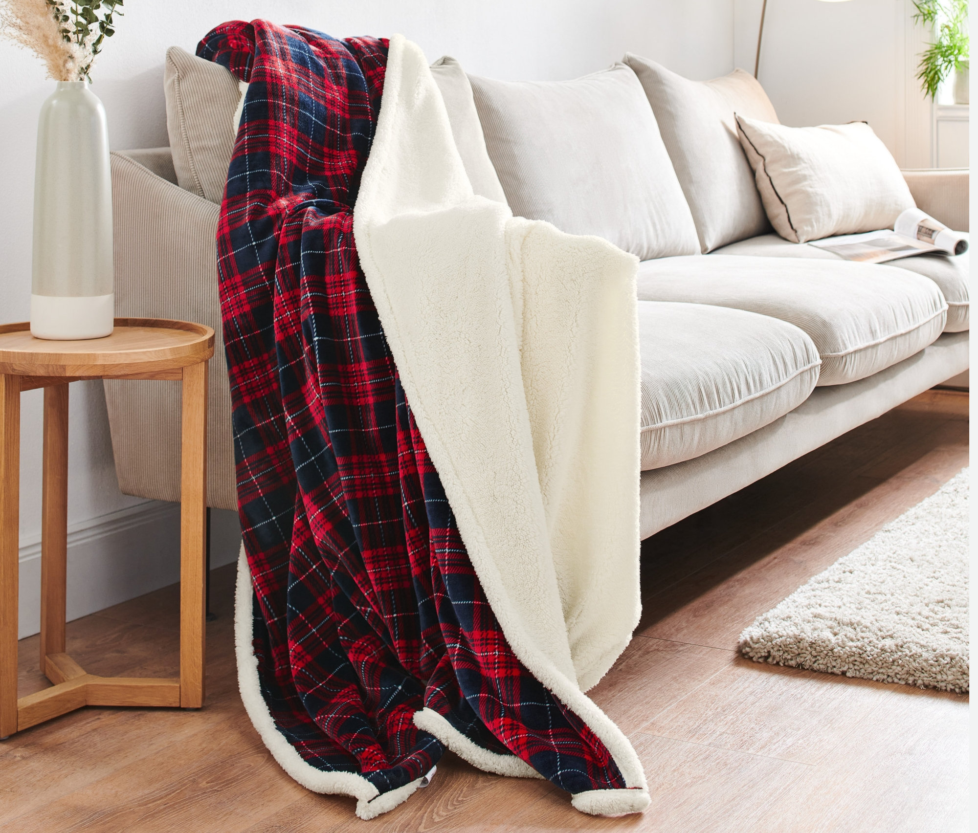 Kırmızı ve mavi kareli Çift Taraflı Battaniye bej renkli bir kanepenin üzerine örtülmüştür.