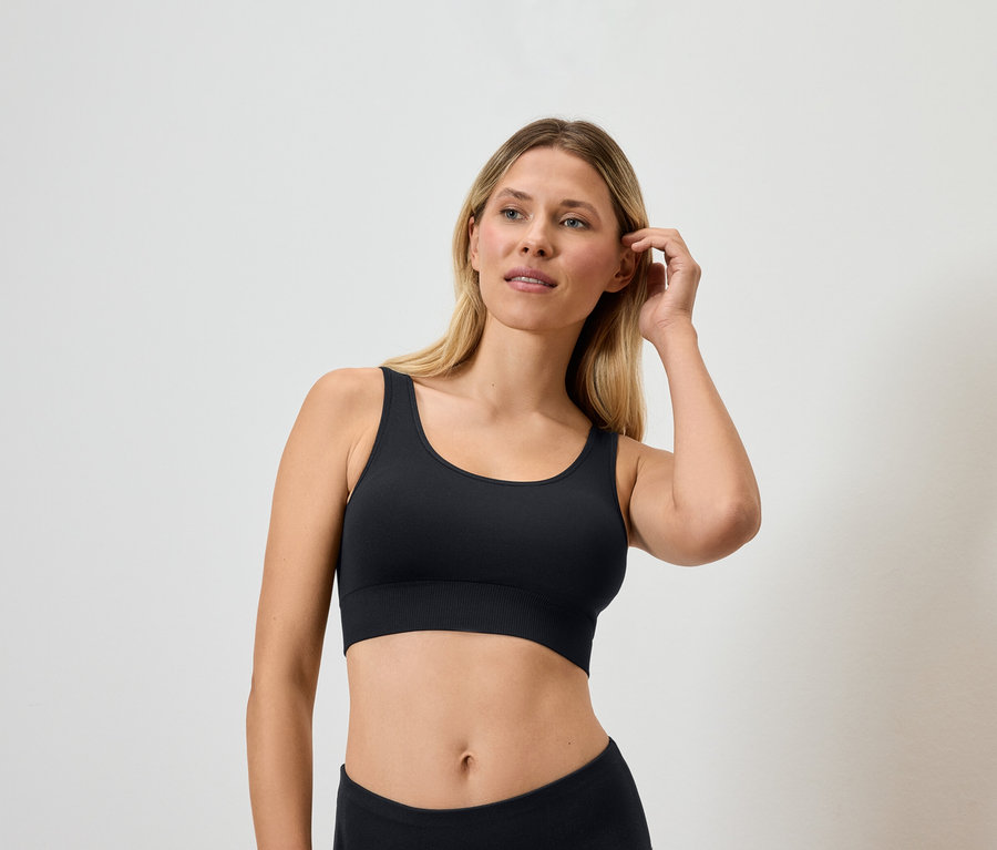 Sarışın bir kadın siyah spor sütyeni giymiş saçına dokunuyor.