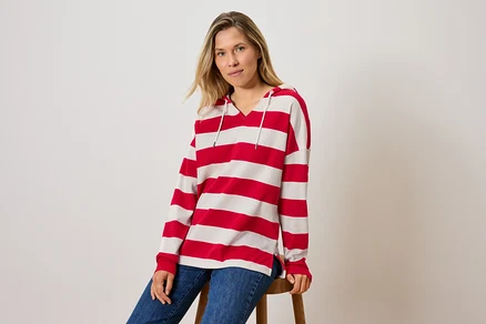 Bir kadın taburede oturuyor, çizgili kapüşonlu bir sweatshirt ve kot pantolon giyiyor.