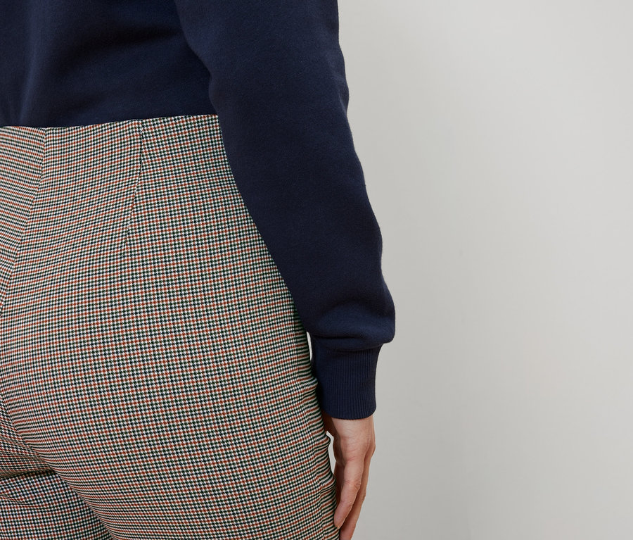 Arkadan bir kadın, lacivert bir kazak ve kareli bir pantolon giyiyor.