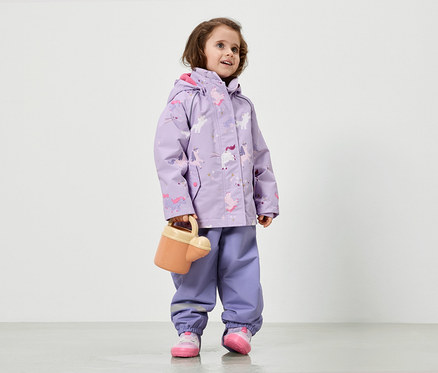 Lilac renkli, tek boynuzlu at desenli yağmurluk giyen bir kız çocuğu sulama kabı tutuyor.