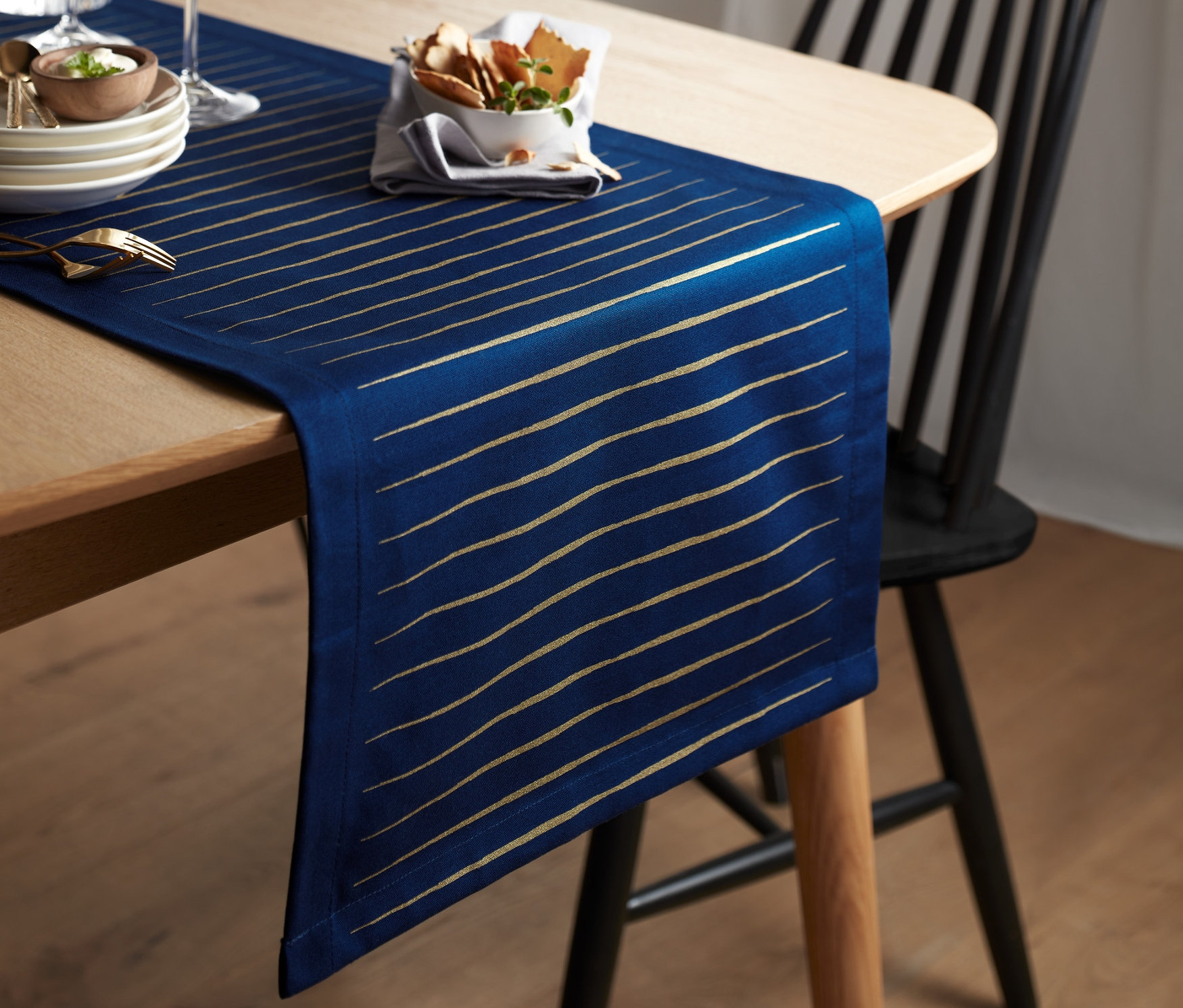 Masanın üzerinde altın şeritli, mavi organik pamuklu şerit örtü bulunuyor.