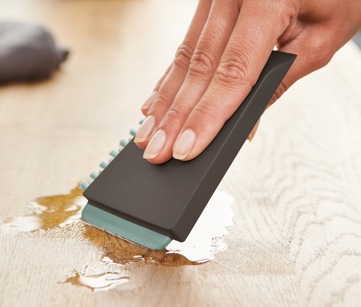 Bir kadın, ahşap bir yüzeydeki sıvıyı Üniversal Mutfak Fırçası ile siliyor.