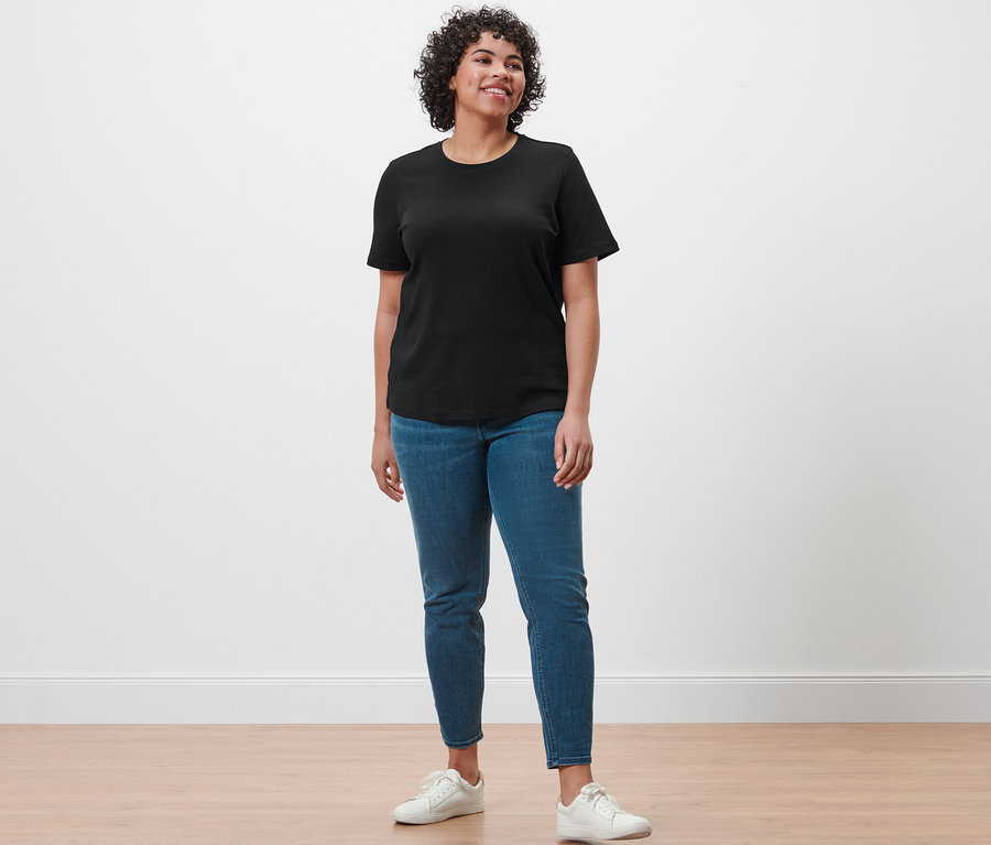 Bir kadın ayakta duruyor, üzerinde siyah Basic T-Shirt, Treggings »Fit Nelly« ve beyaz spor ayakkabılar var.