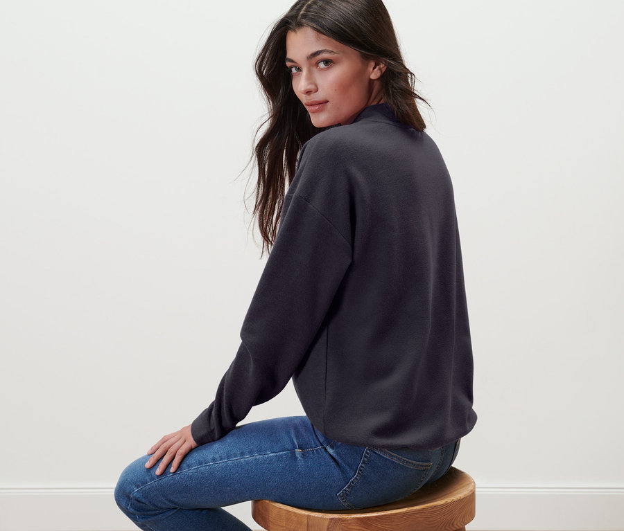 Bir kadın taburede oturuyor ve Yarım Balıkçı Yaka Sweatshirt giyiyor.