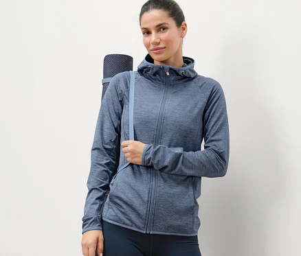 Kadın kırçıllı mavi spor mont giyiyor ve yoga matı taşıyor.