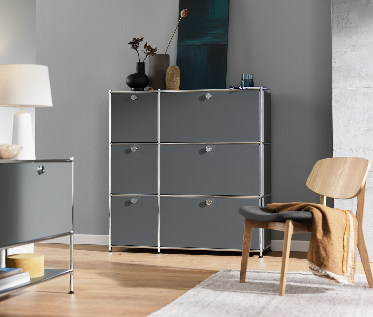 İç mekanda gri »CN3« 6 kapaklı komodin, gri »CN3« 1 kapaklı yan sehpa, beyaz masa lambası ve Lounge Sandalyesi bulunmaktadır.