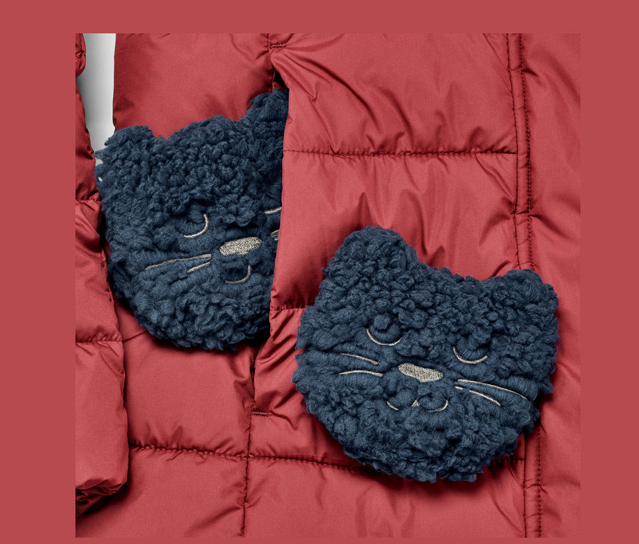 Kırmızı bir ceketin üzerinde iki adet »Kedi« cep ısıtıcısı bulunmaktadır.