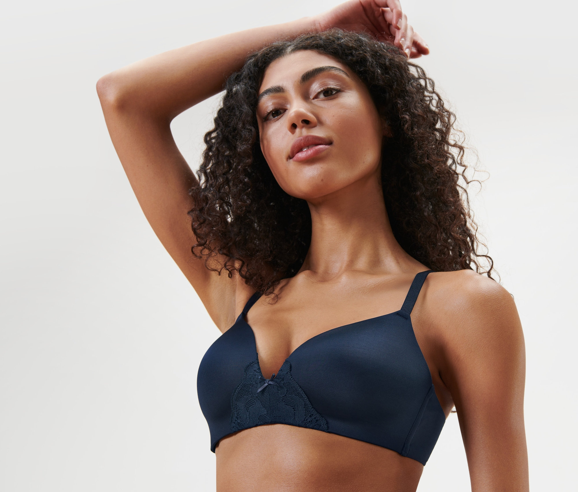 Başı üzerinde bir eli olan bir kadın mavi, yumuşak kuplu bir sütyen giyiyor.