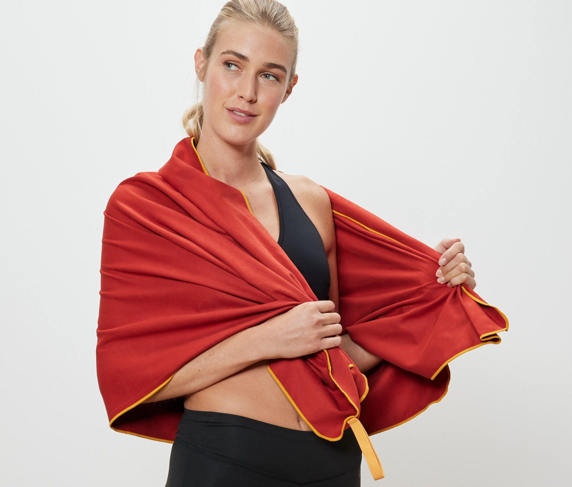 Sarışın bir kadın, yaklaşık 70 x 140 cm boyutlarındaki turuncu renkli outdoor havluyu omuzlarına atıyor.