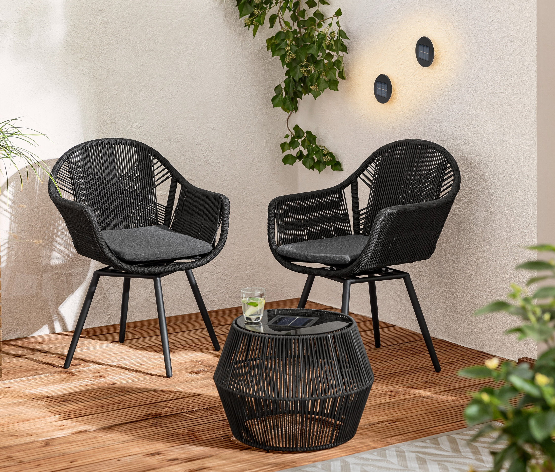 Ahşap terasta iki adet Kumaş Örgülü Döner Yemek Sandalyesi ve Tekstil Bantlı Güneş Enerjili Sehpa bulunmaktadır. Duvarda 2 adet solar duvar ve basamak lambası var.