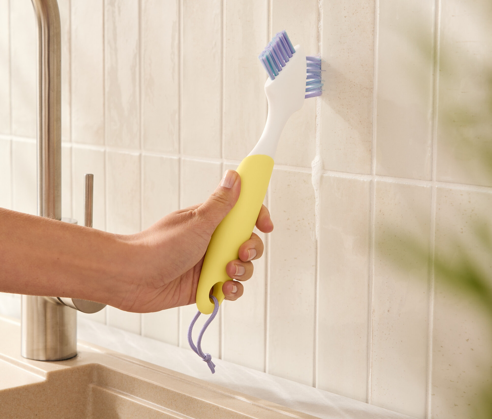 Bir el sarı bir fayans fırçası tutuyor ve fayanslar arasındaki derzleri temizliyor.