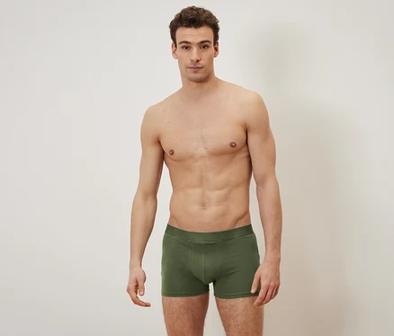 Üstü çıplak bir adam zeytin yeşili boxer külotla poz veriyor.