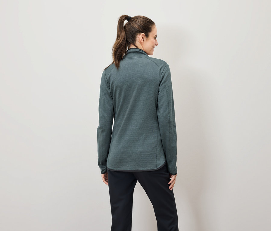 Arkadan bakıldığında, kahverengi saçları at kuyruğu yapılmış, yeşil fermuarlı bir sweatshirt ve siyah pantolon giyen bir kadın görülüyor.