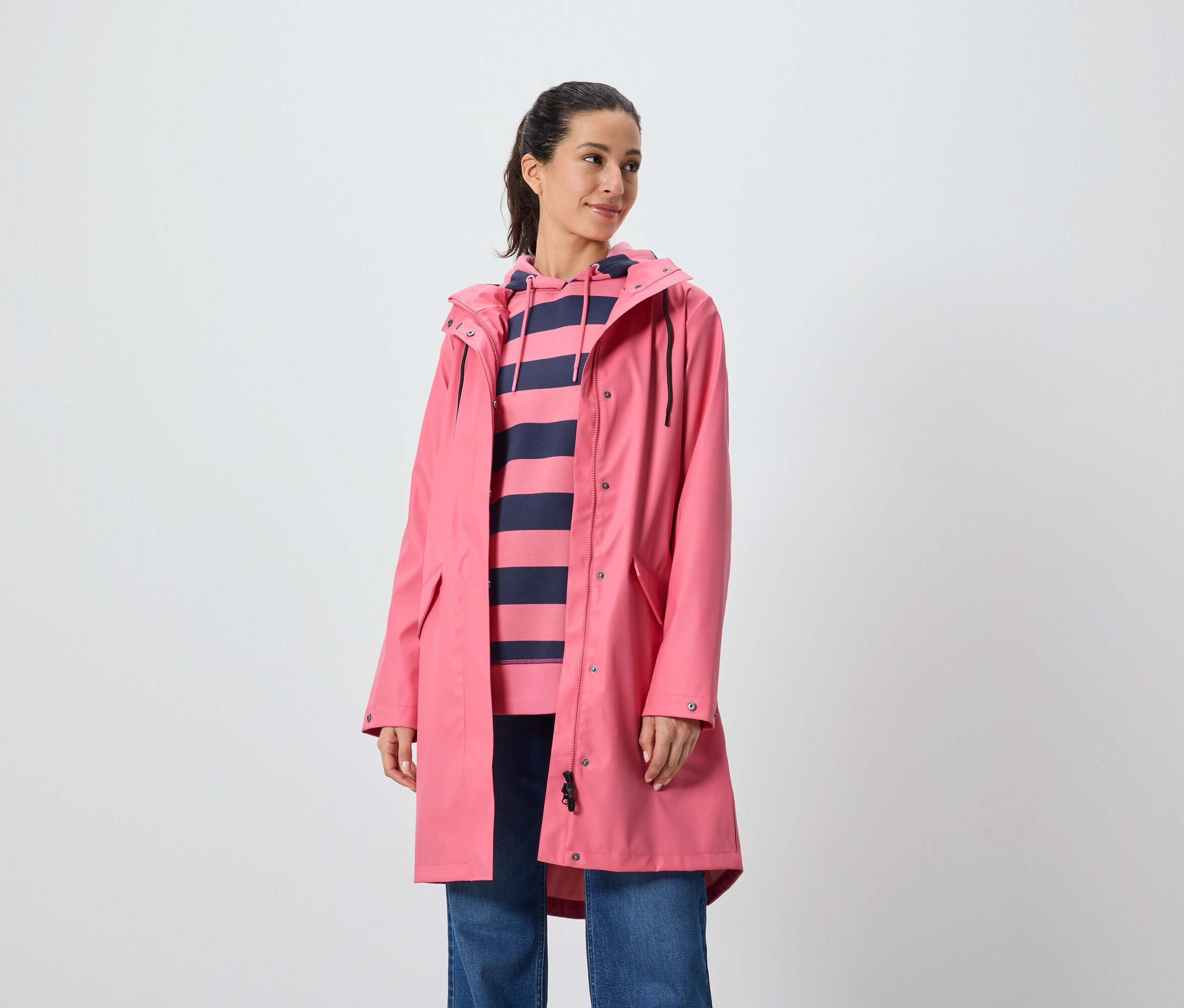 Kadın pembe bir palto ve çizgili kapüşonlu bir sweatshirt giyiyor.