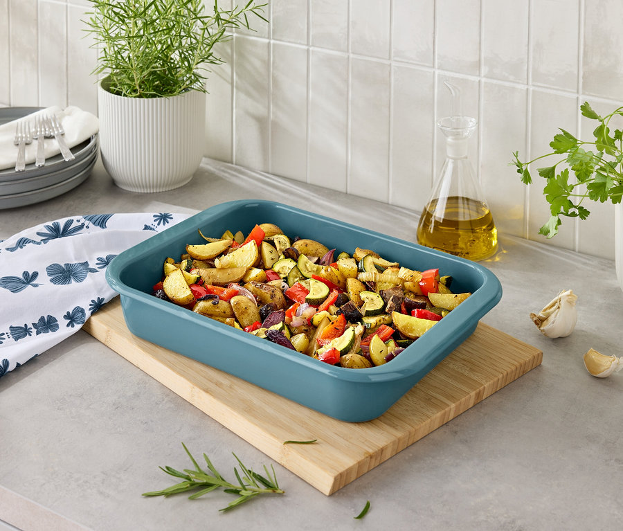 Tahta bir kesme tahtası üzerinde mavi bir fırın kabında sebzeli fırında patates.