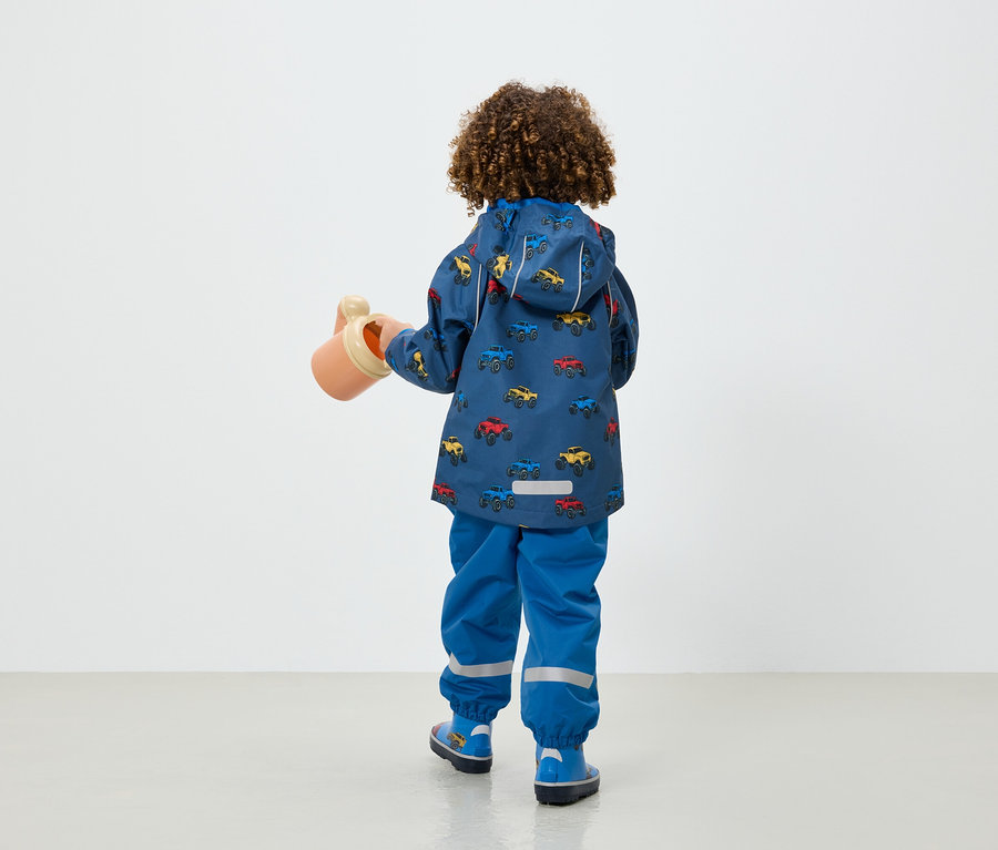 Araba baskılı mavi ceket ve pantolon giyen bir çocuk bej renkli bir sulama kabı tutuyor.