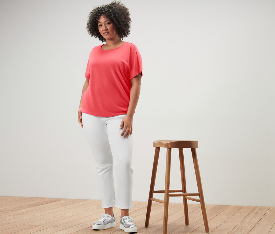 Kadın ahşap taburenin yanında duruyor ve mercan rengi bir bluz giyiyor.