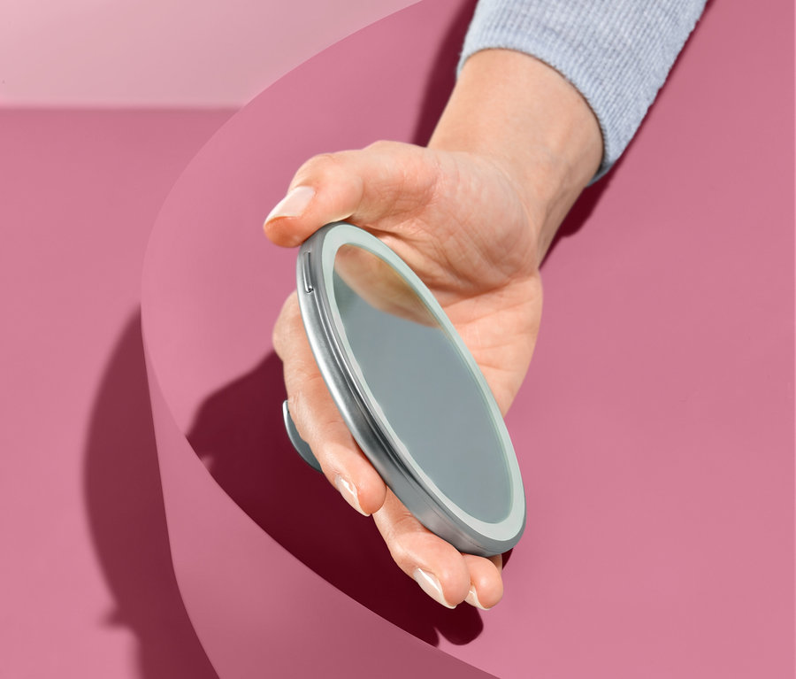 El, pembe bir arka plan önünde LED Makyaj Aynası tutuyor.