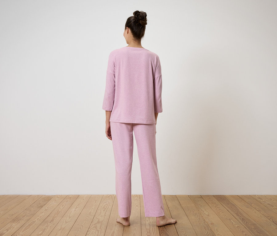 Bir kadın kameraya arkası dönük duruyor ve pembe bir pijama giyiyor.