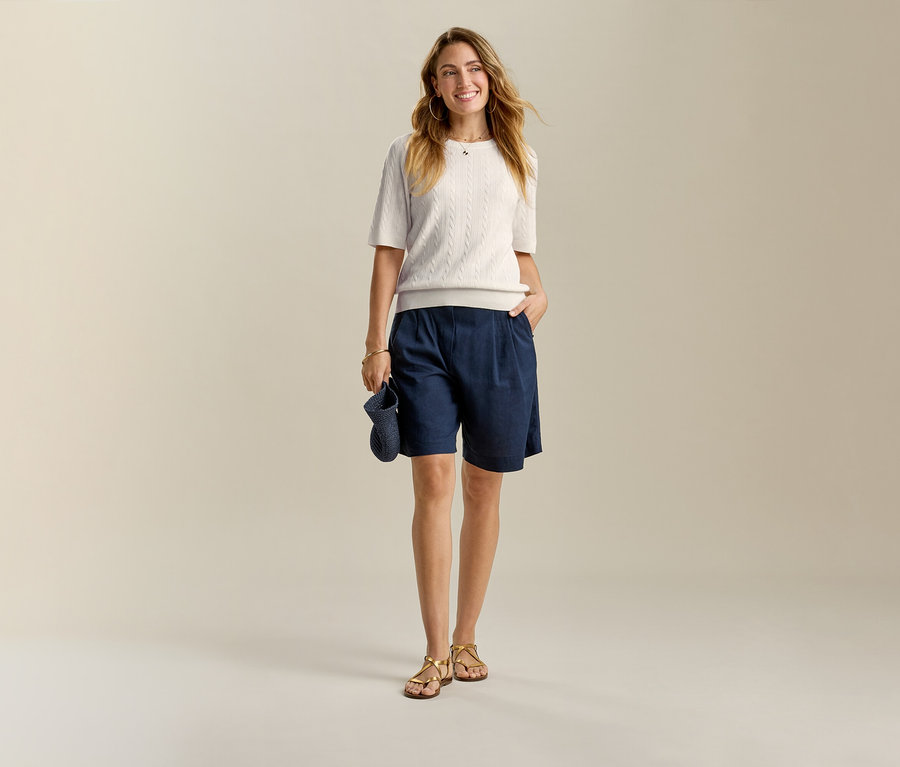 Açık renk üst ve lacivert Leinen-Bermuda-Shorts giyen, eli cebinde bir kadın.