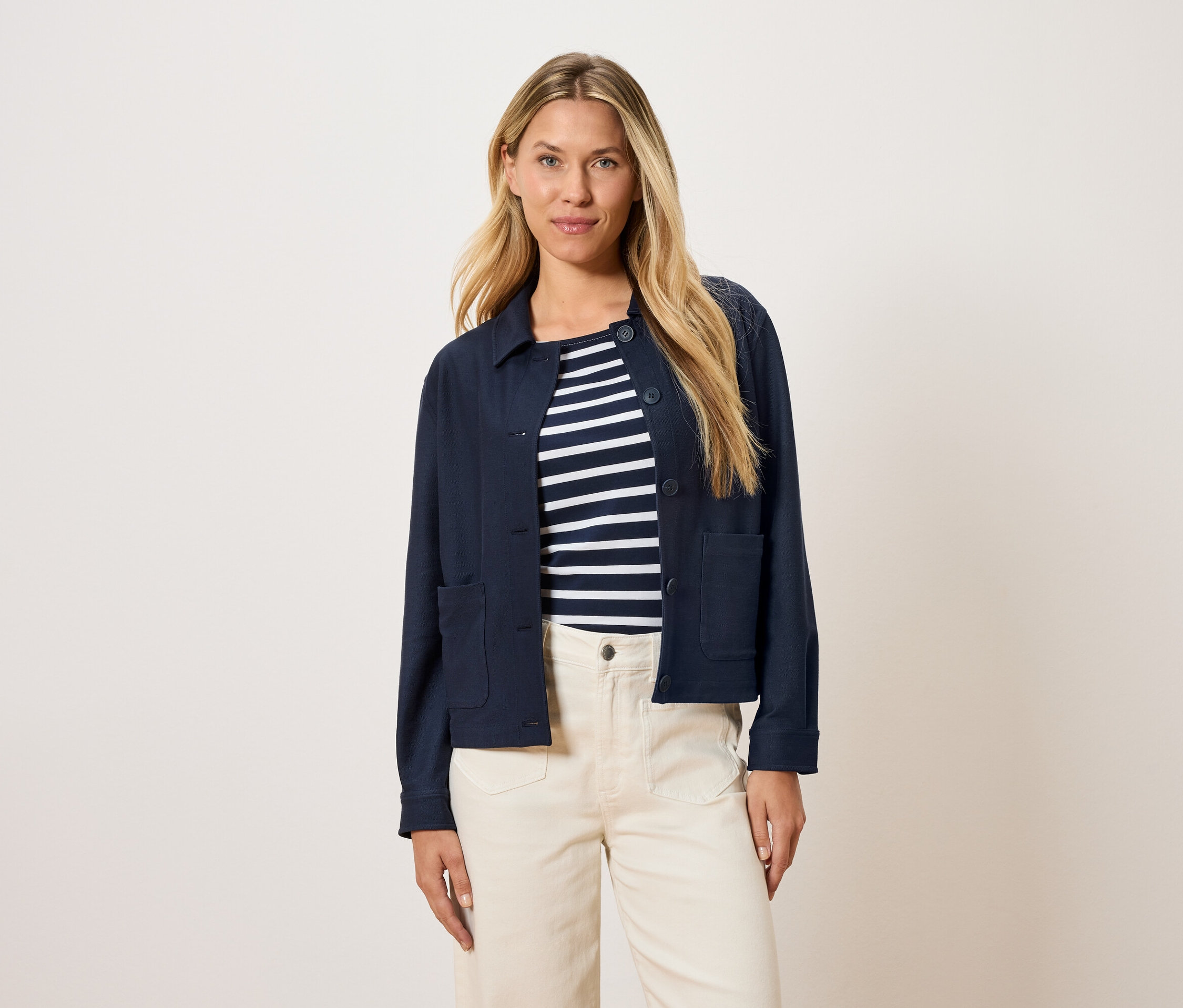 Kadın, çizgili bir üst ve krem rengi pantolon üzerine lacivert bir ceket giyiyor.