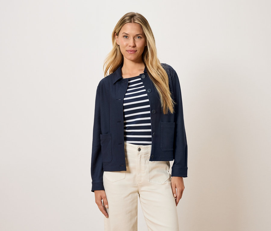 Kadın, çizgili bir üst ve krem rengi pantolon üzerine lacivert bir ceket giyiyor.