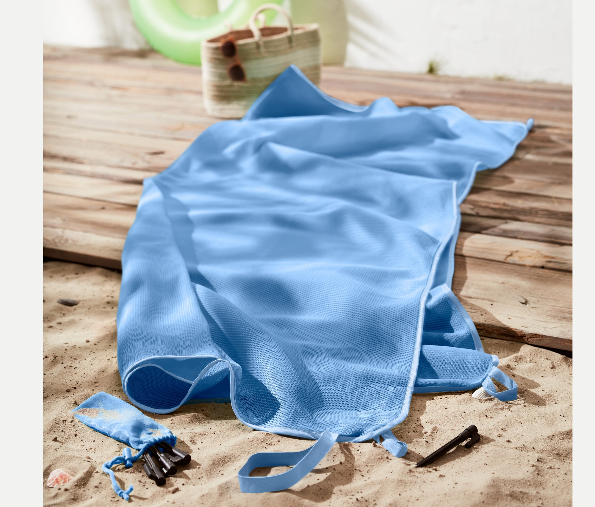 Kum tutmayan açık mavi plaj örtüsü, plaj çantası ve şamandıranın yanında kum üzerinde duruyor.