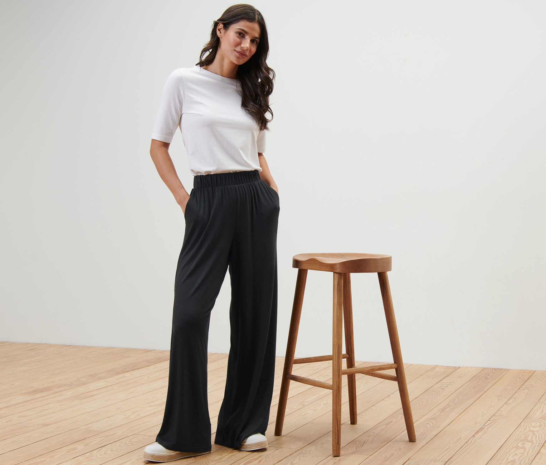 Bir kadın, ahşap bir taburenin yanında siyah Palazzo Pantolon ile poz veriyor.