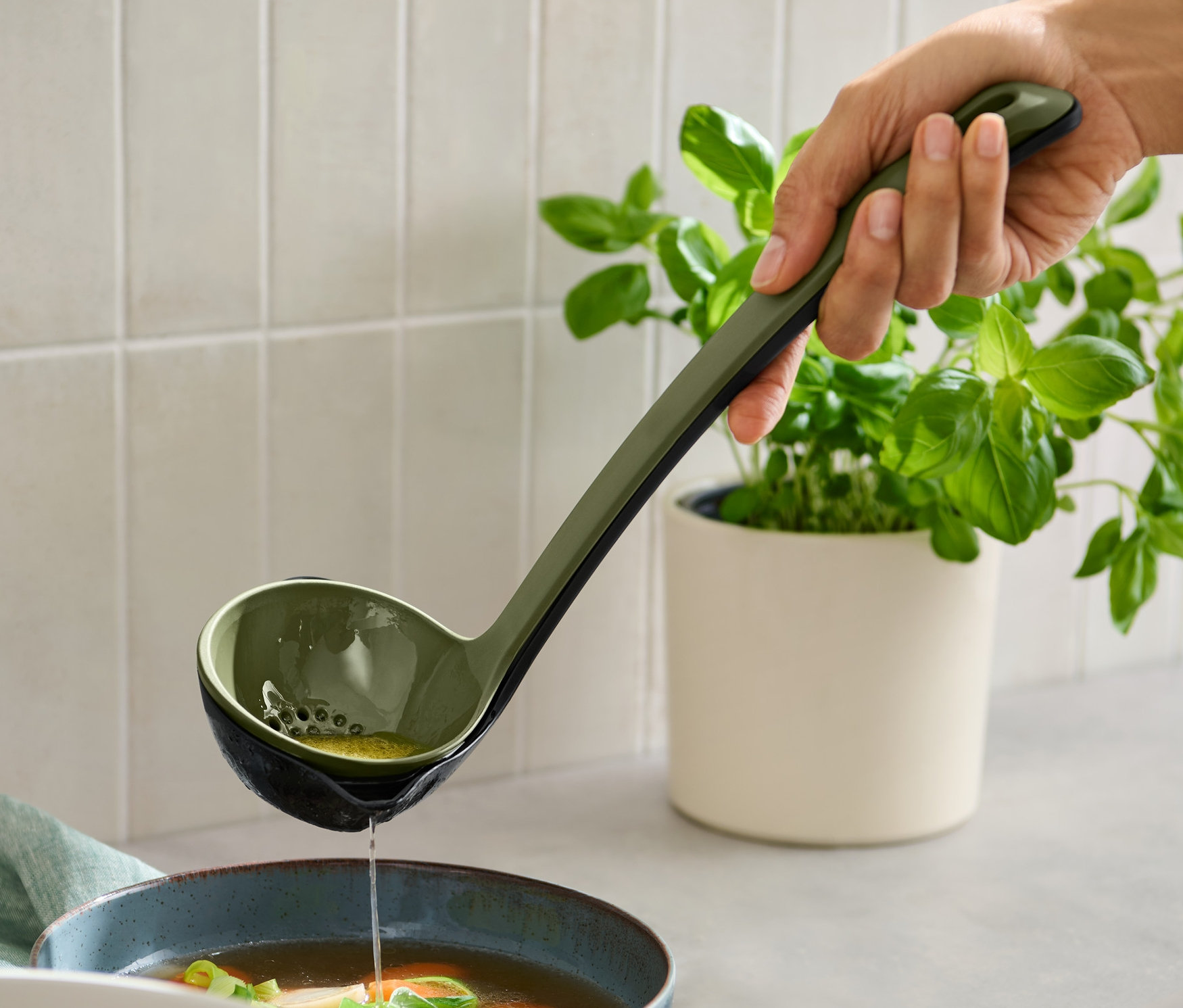 El çorbayı çok amaçlı kepçe ile bir kaseye döküyor.