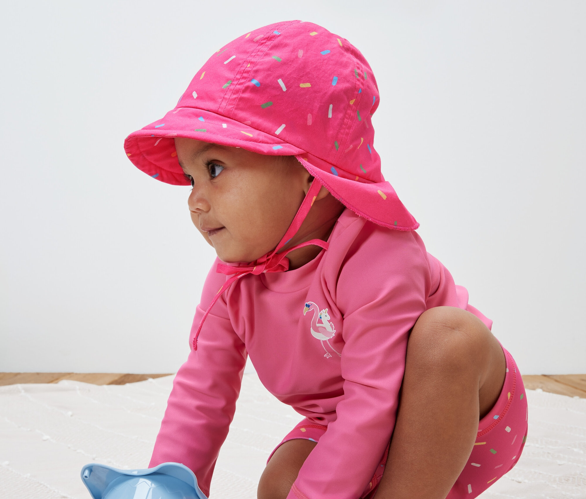 Çocuk oyuncakla oynuyor ve 80 faktörlü pembe bir güneş şapkası takıyor.