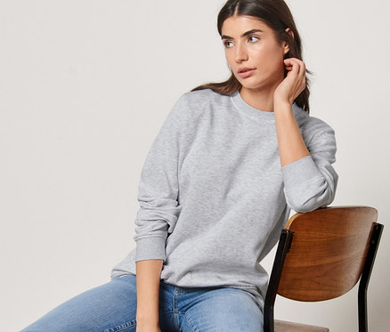 Kadın sandalyede oturuyor ve gri bir sweatshirt giyiyor.