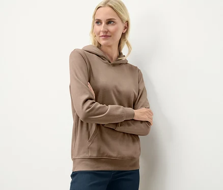 Sarışın bir kadın, bej rengi kapüşonlu bir sweatshirt ile kolları çapraz şekilde poz veriyor.