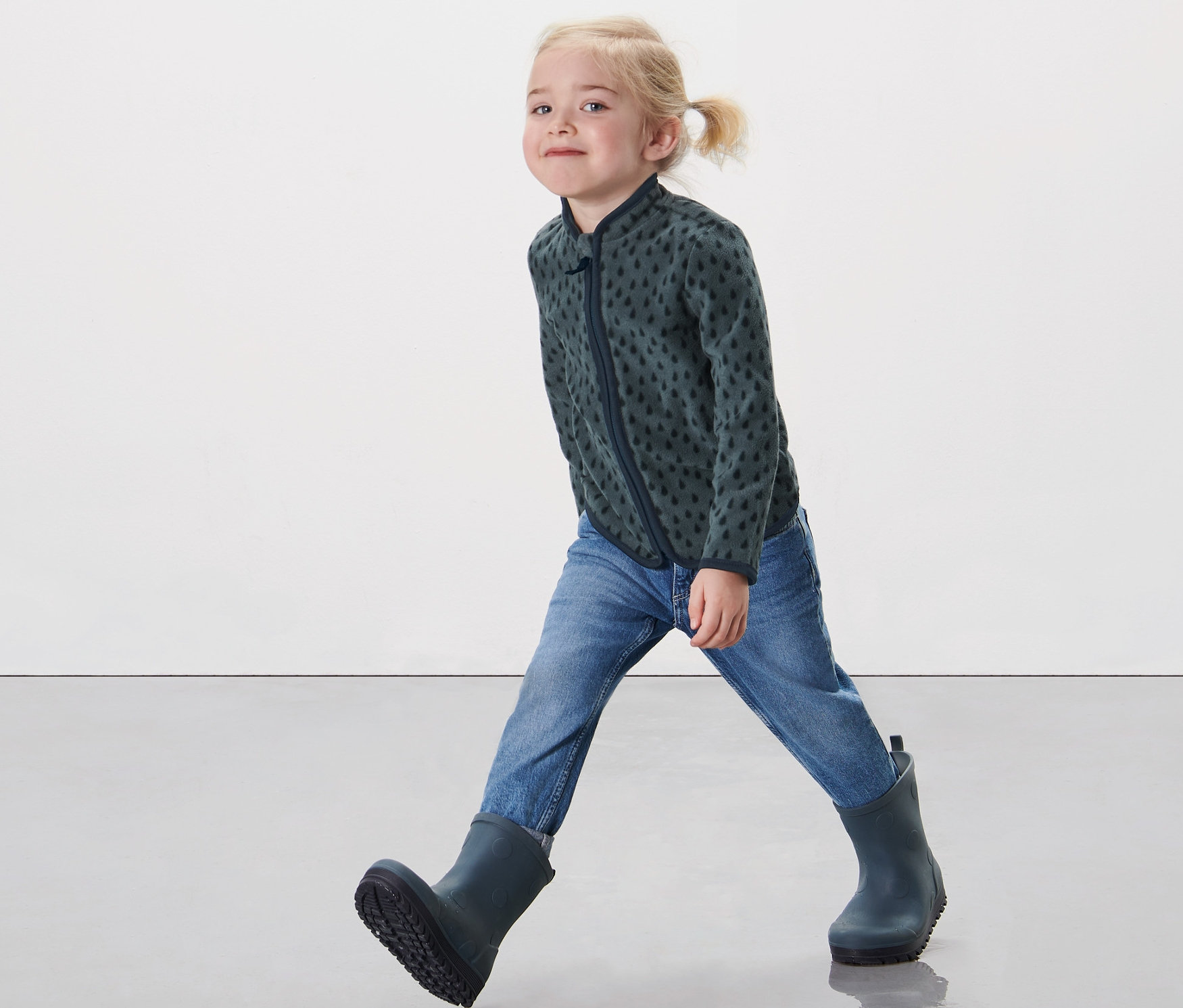 Küçük bir kız çocuğu Küçük Çocuk Polar Ceket, Damla, kot pantolon ve lastik çizme ile yürüyor.